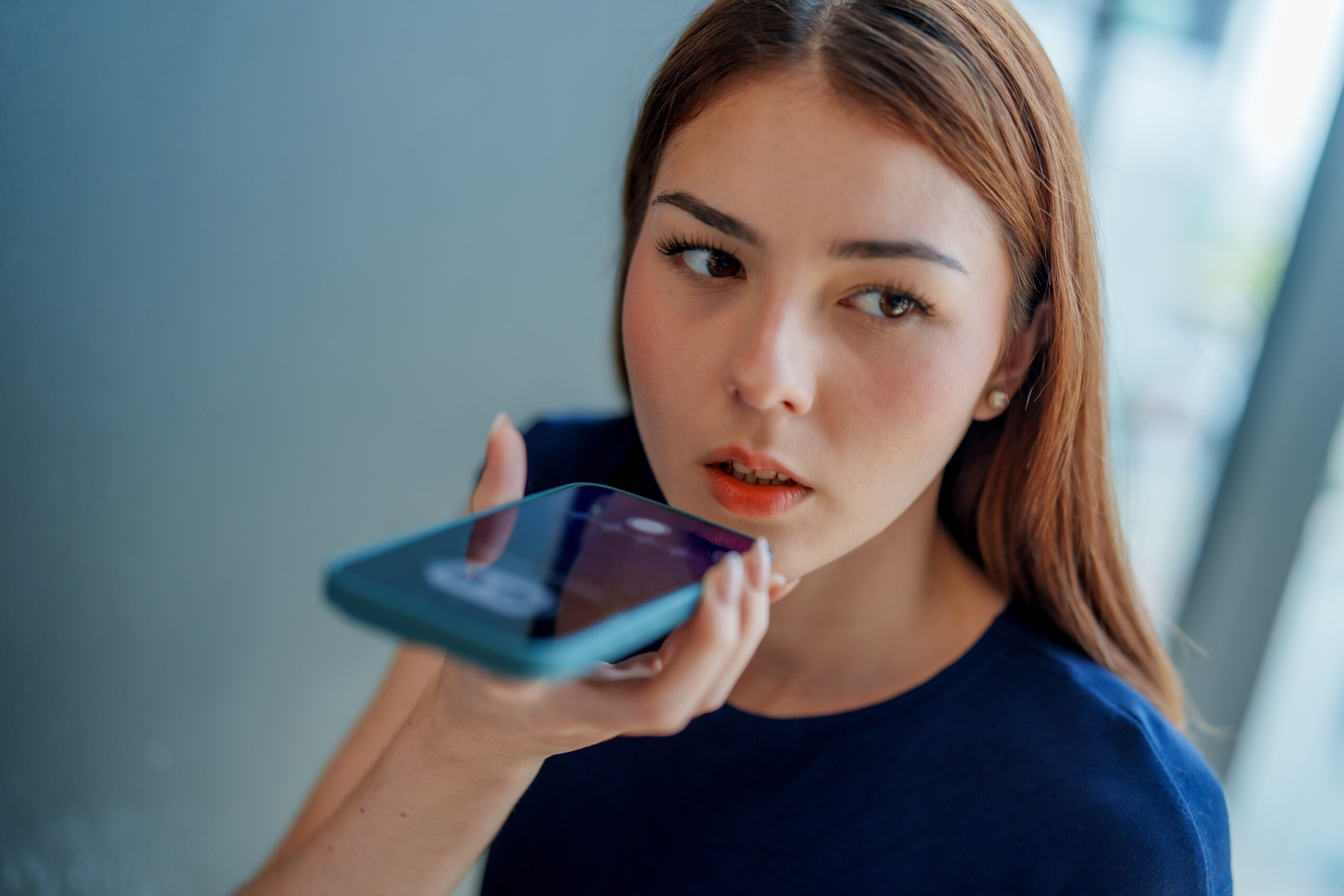 Young woman is using smartphone to interact with chatbot assistant, showcasing integration of AI technology in daily life. Her expression reflects curiosity and engagement